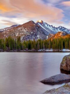 Snow capped mountains on the other side of a still lake. Dusk created a purple glow over the landscape.