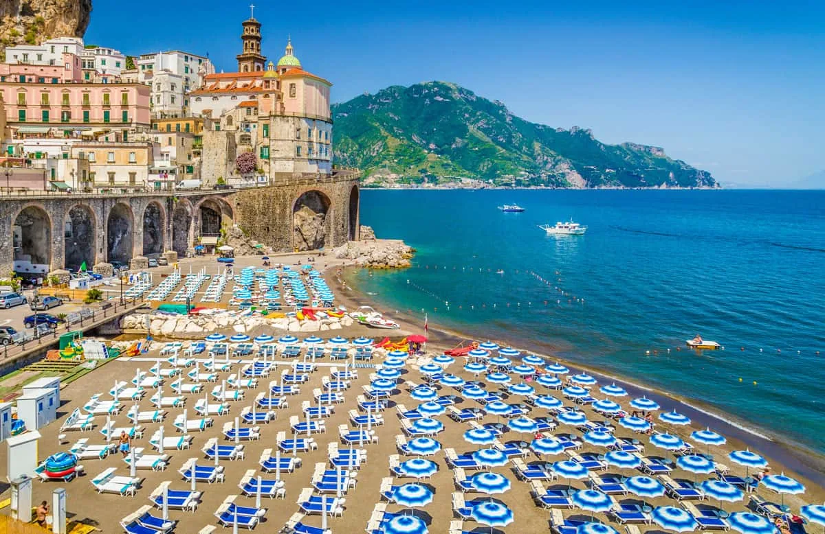 Blue and white beach umbrellas below pastel buildings on the Amalfi Coast.