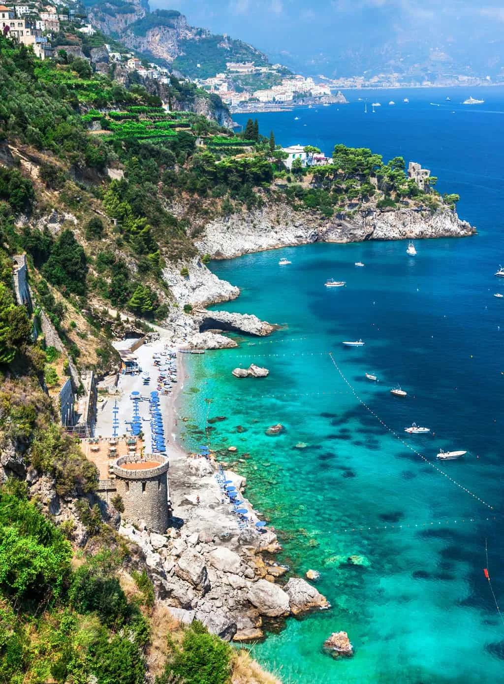 Bright turquoise sea with boats moored in front of a small beach on the rugged coast of the Amalfi.
