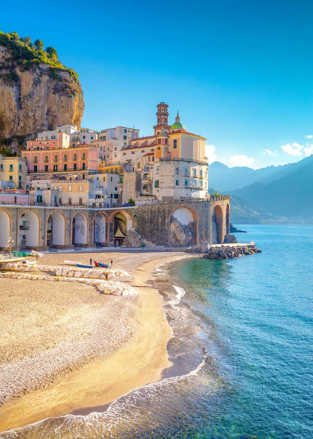 A calm white beach at sunrise in front of pastel buildings on the Amalfi Coast in Italy.