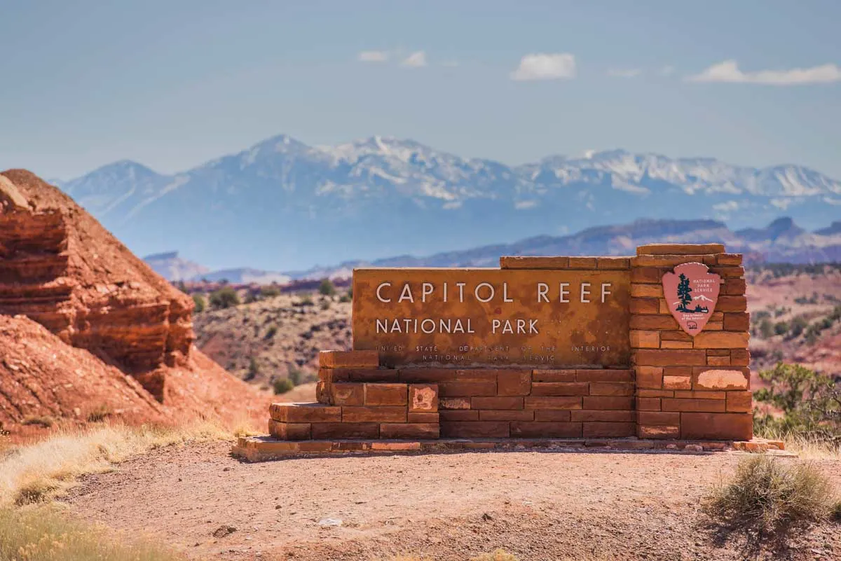 The entry sign to Capitol Reef National park surrounded by rocky, mountainous landscape.