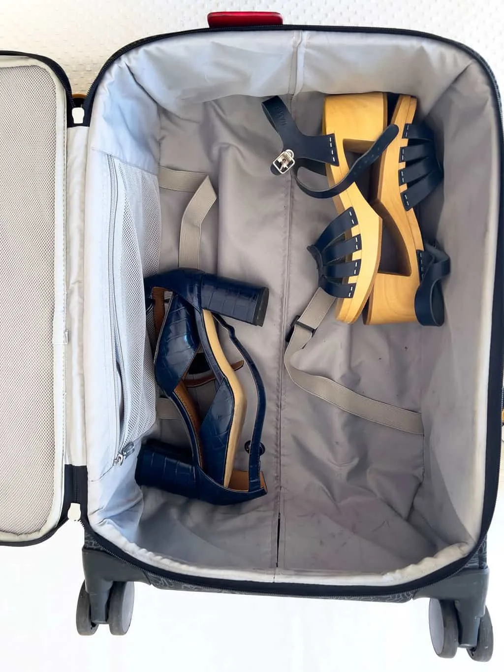 Two pairs of ladies heels in a grey suitcase. They are at opposite corners of the suitcase on their side. Both shoes are navy blue. 