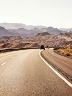 Two cars on an empty highway to Las Vegas. The landscape is red rocky and barren.