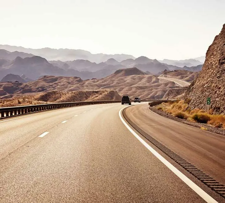 Two cars on an empty highway to Las Vegas. The landscape is red rocky and barren.