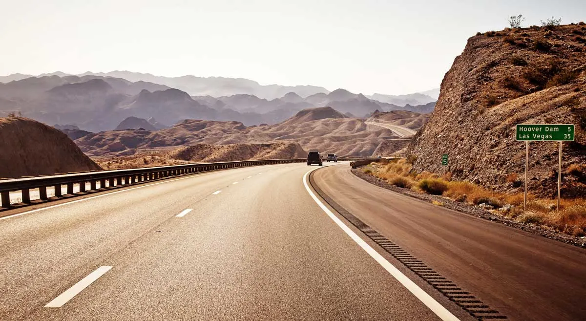 Two cars on an empty highway to Las Vegas. The landscape is red rocky and barren. 