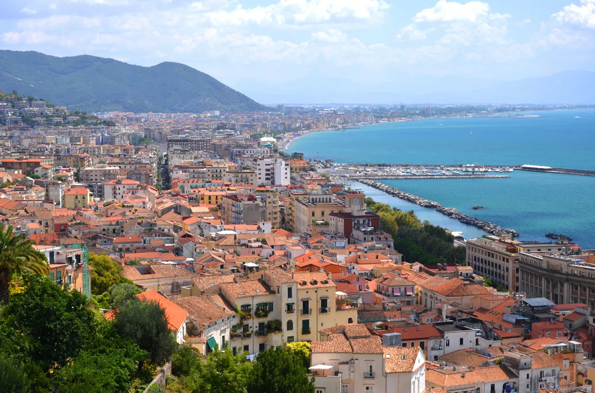 A view over the coastal town of Salerno which traces the blue coast with mountains in the distance. 