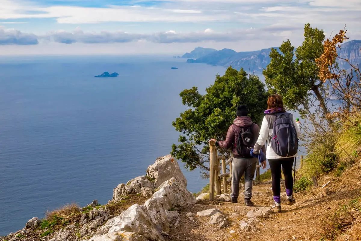 Two hikers stand at a lookout point looking at the views over the Amalfi Coast.