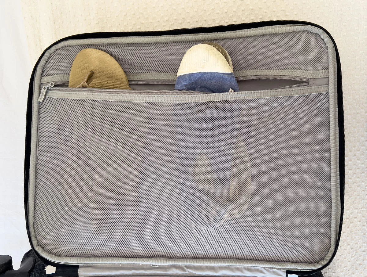 FLip flops and a pair of sneakers in the mesh pocket of a suitcase. 