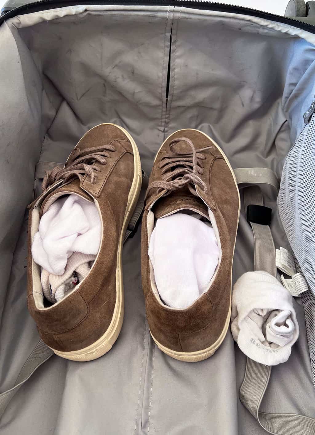 A pair of brown suede sneakers in a suitcase. The sneakers are stuffed with white socks. 
