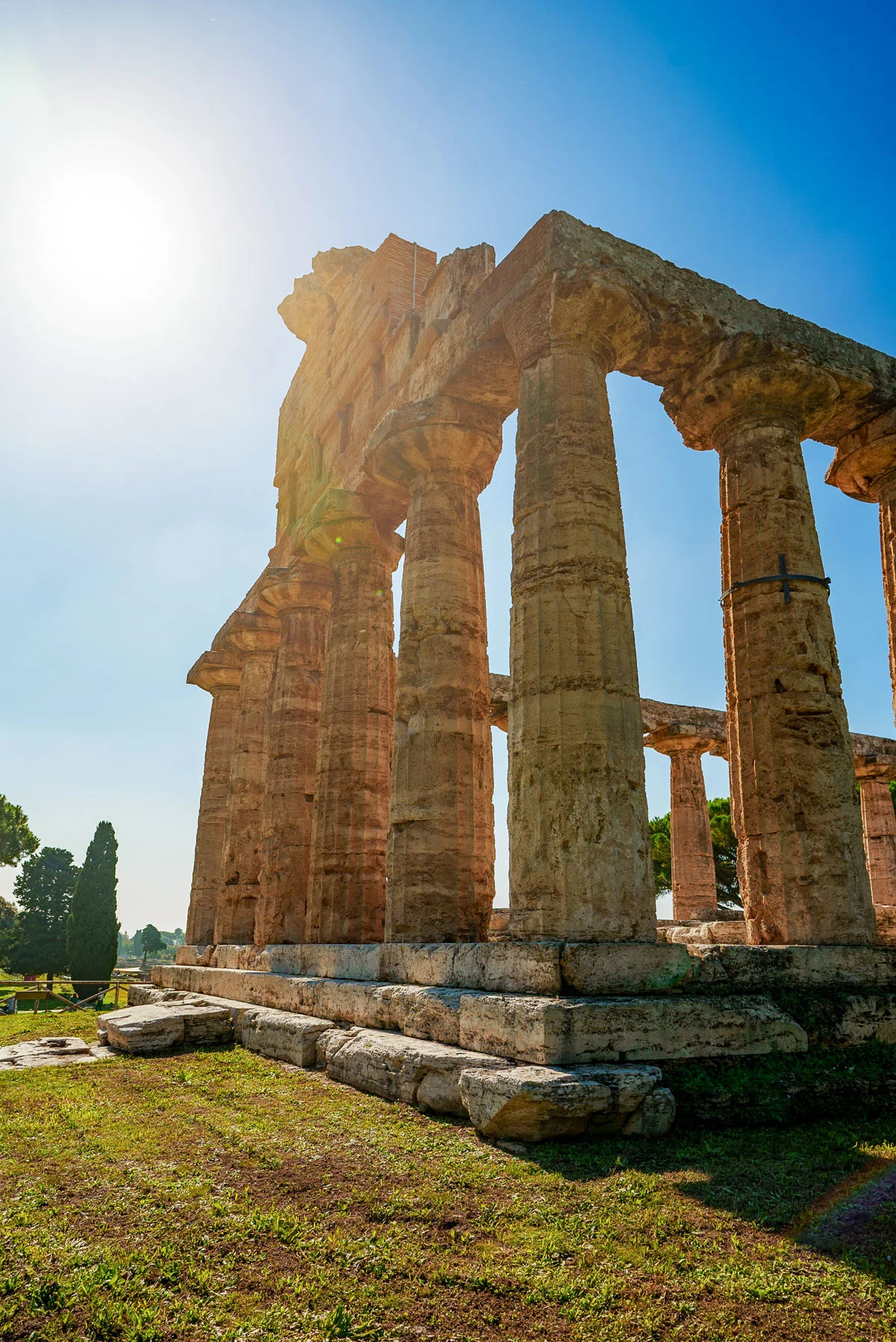 The sun shining down on ancient Greek temple ruins framed by a blue sky. 