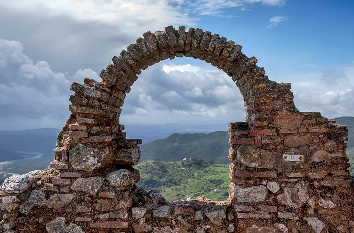 Looking through an archway of a castle ruin across the Spanish countryside with a dramatic sky. 