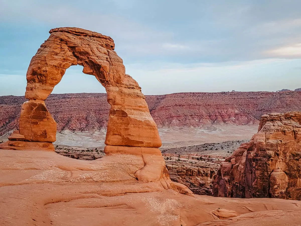 A natural rock arch overlooking a red rocky canyon landscape. 