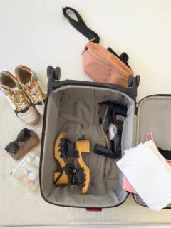 A flat lay image of a suitcase on a bed with women's clothing and shoes being packed. There are lots of pink items.