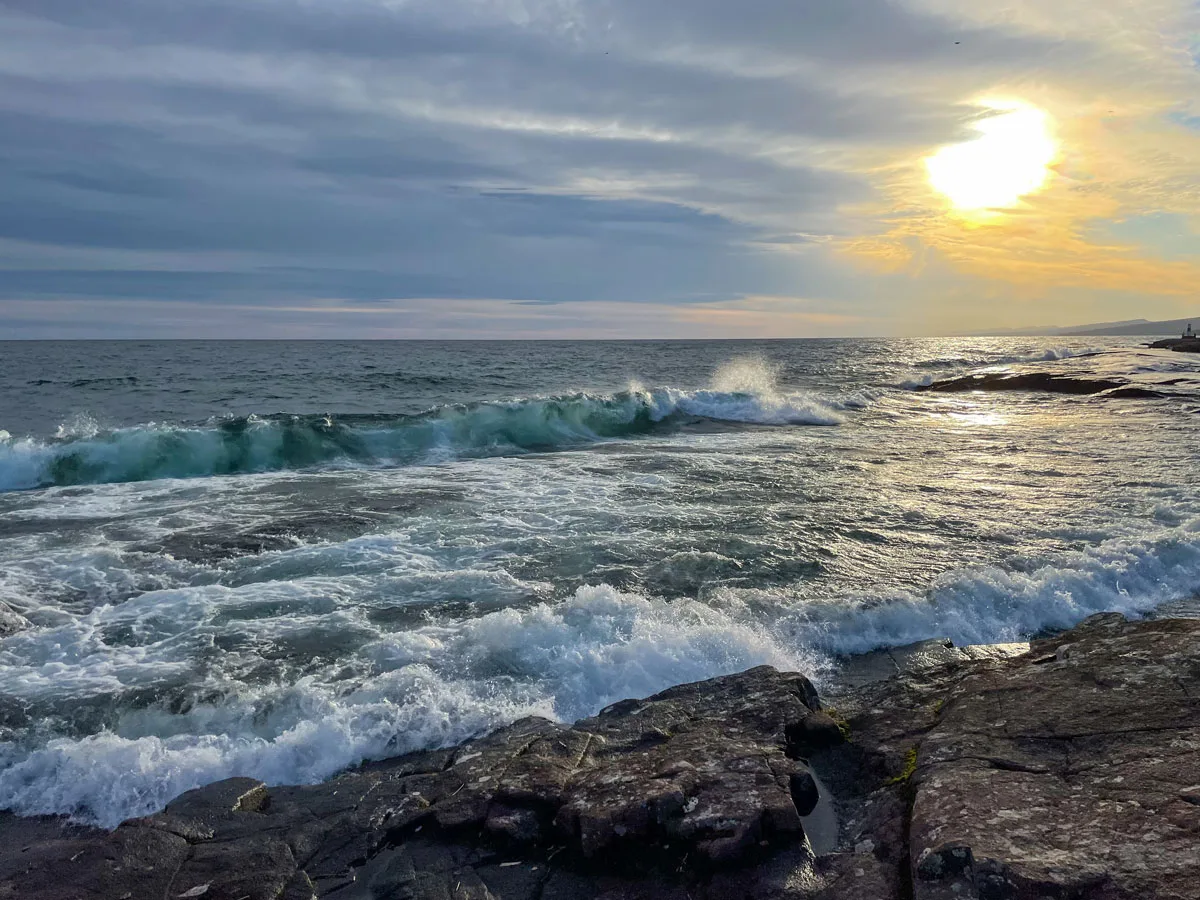 Sun setting over the coast with waves washing up on shore. 