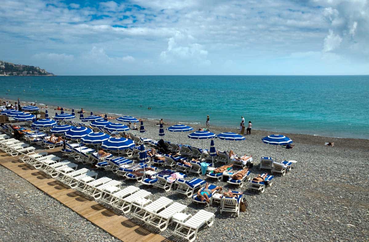 Sun lounges with blue and white umbrellas on a beach in Nice France.