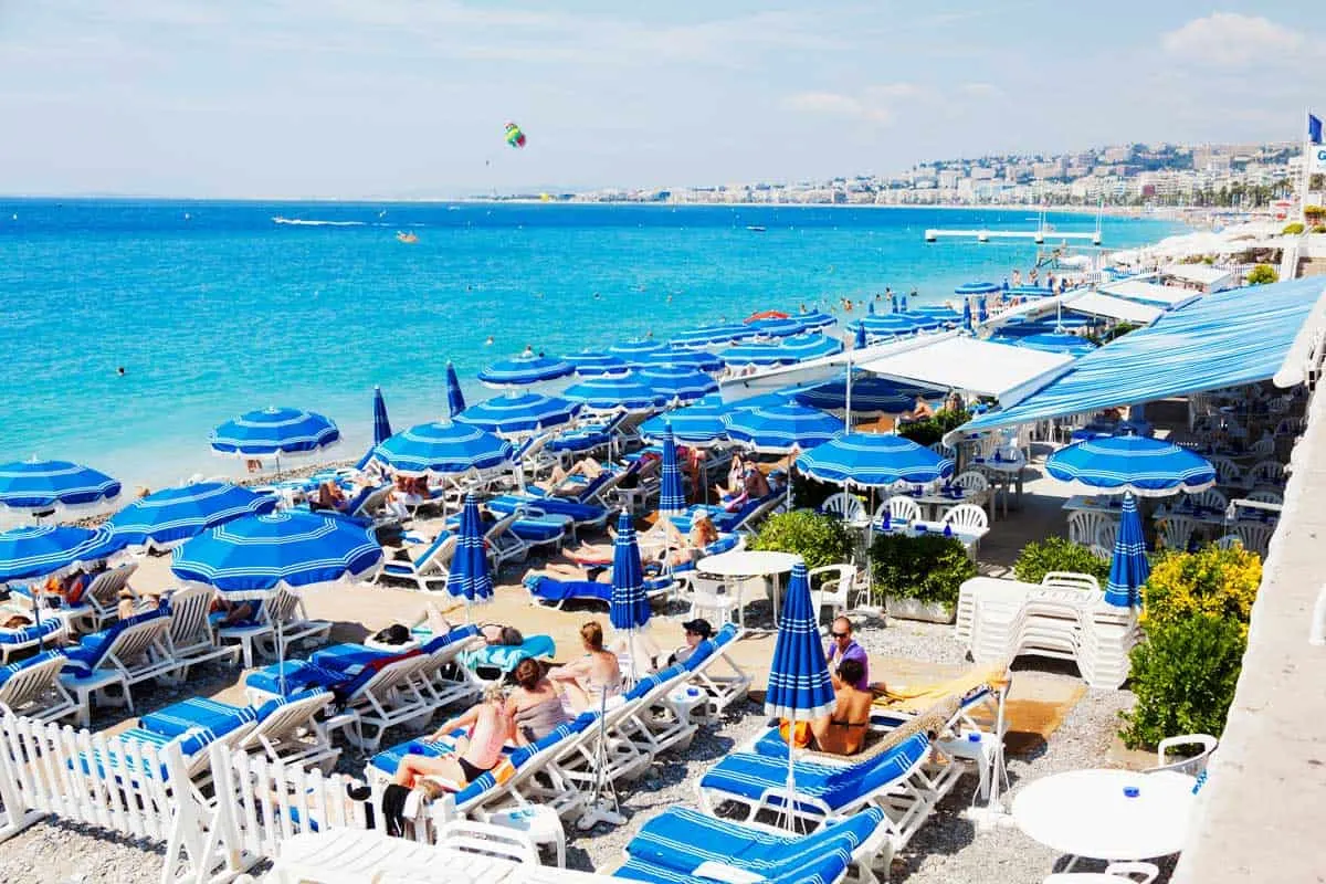 A crowded beach in nice with lots of blue and white beach umbrellas. 