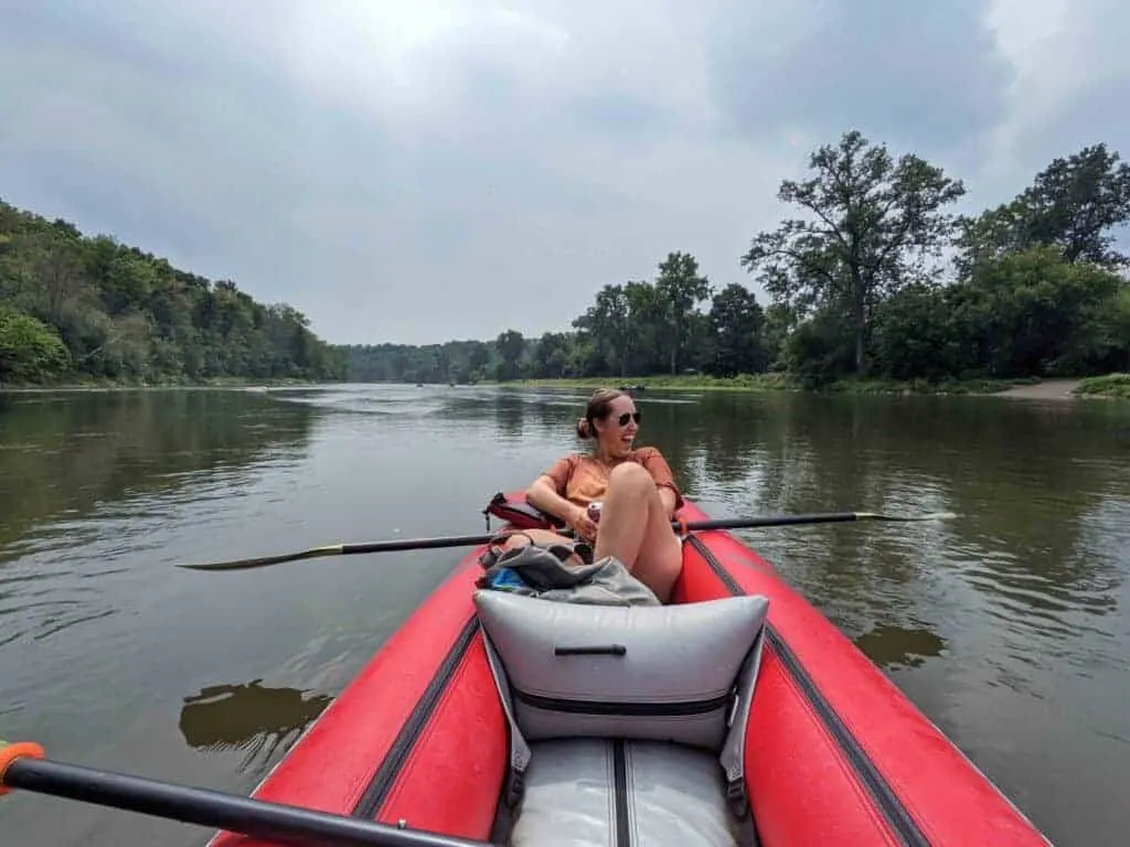 A girl floating down a river in a red canoe. 