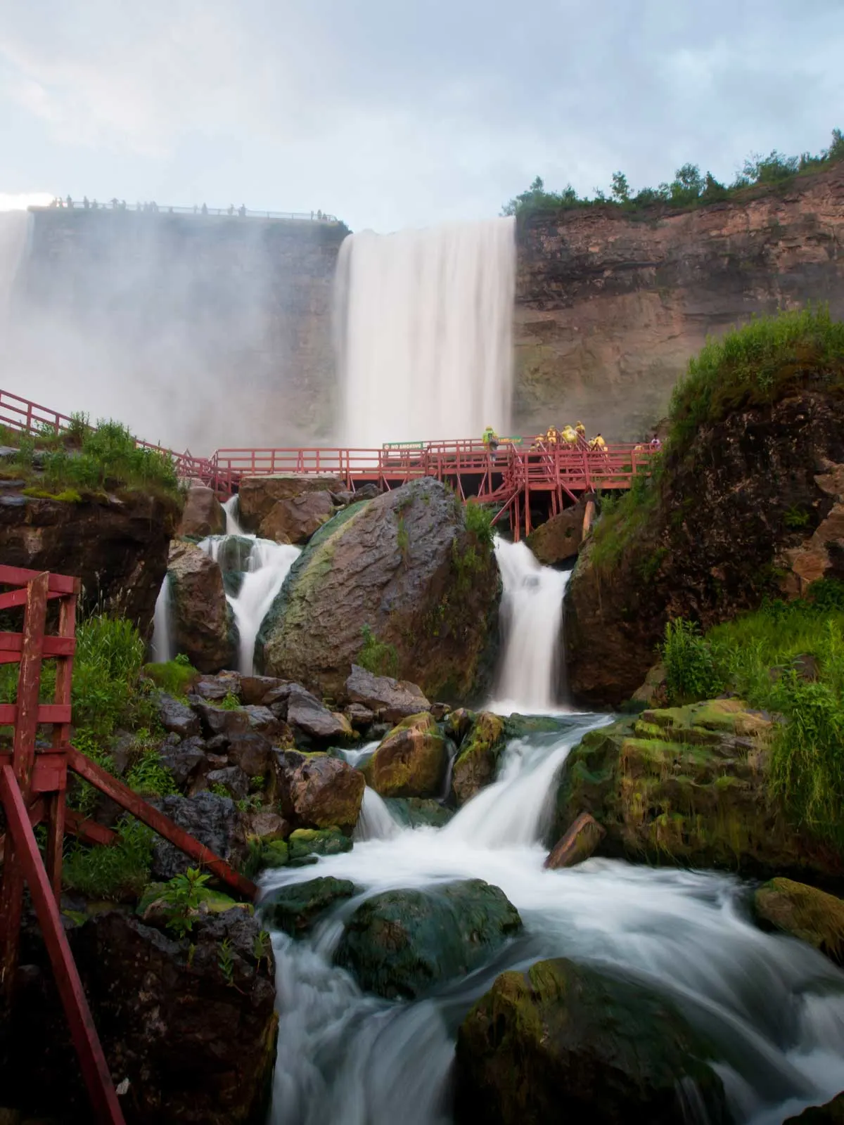 Tourists standing on a red bridge in front of Niagara Falls.