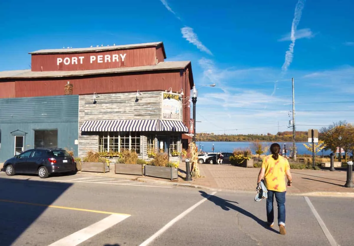 Man on a pedestrian crossing of the main street of Port Perry near the waterfront with historic building.