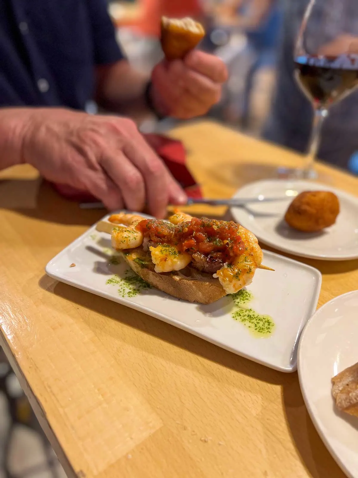 Close up of a mans hands eating tapas and a glass of red wine. 