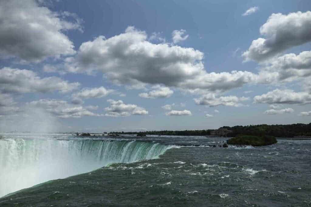 Water gushing over the top of Niagara Falls with clouds in the sky. 