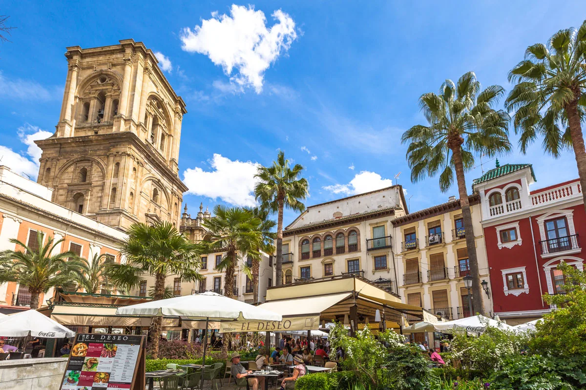 Typical Spanish buildings and the cathedral tower surround a plaza in Granada Spain. 