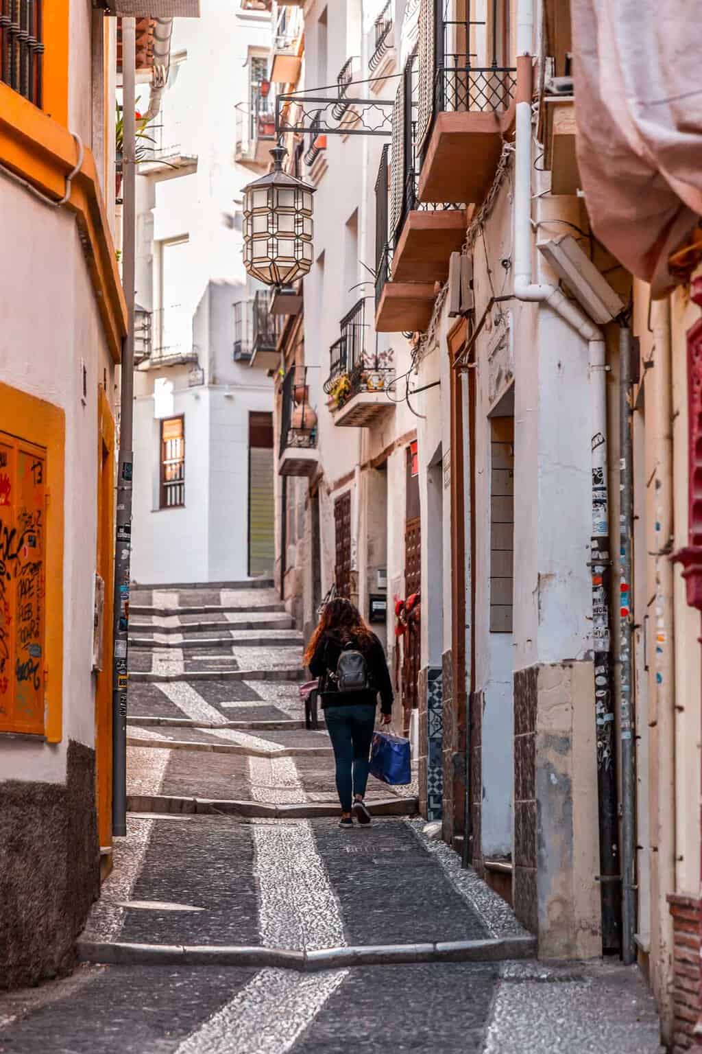 A girls walks up a narrow street in the old town of Granada Spain. 