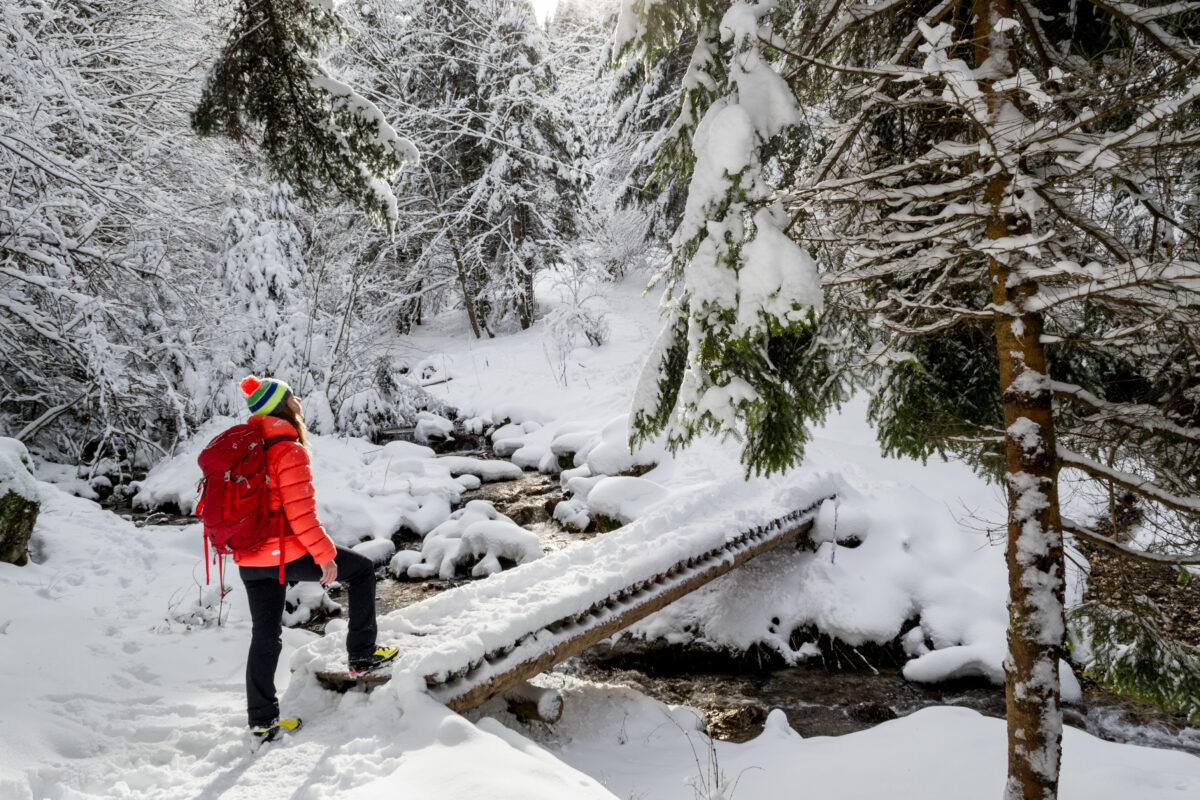Backpacking female hiker going over a snow covered bridge in the winter
