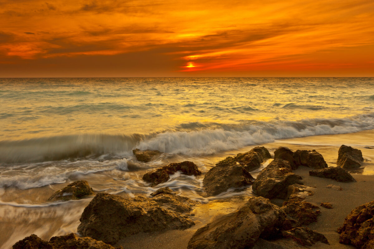 Sunrise at Beach at Venice Beach, Florida. Orange and pinks skies over waves and rocks on beach