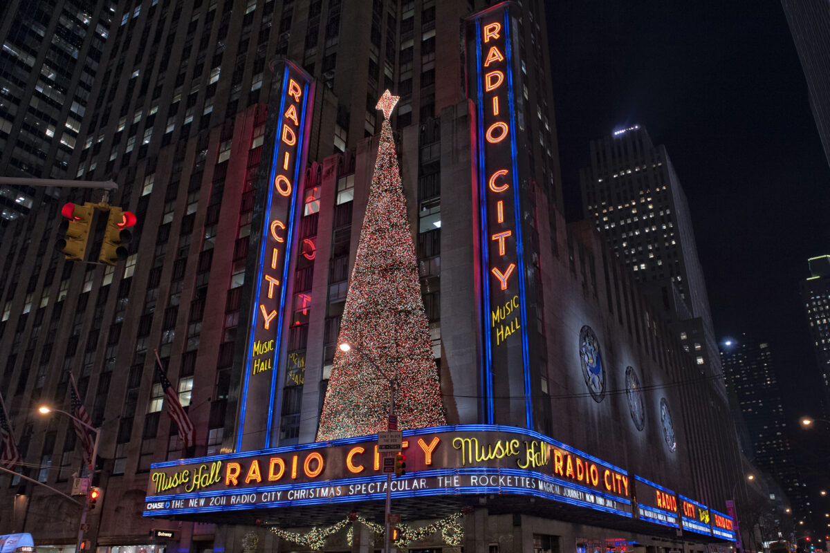 Outside Radio City Music Hall, Rockettes at Christmas time in New York. Building with lit Christmas tree up top in the evening