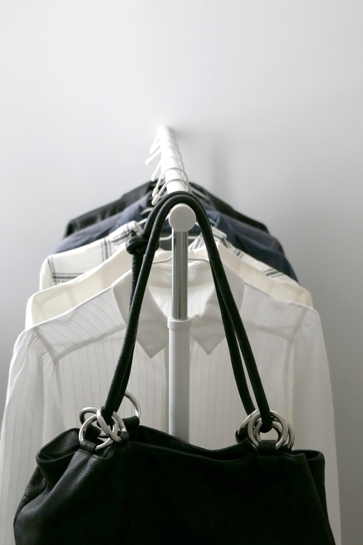 A purse with several white, blue and black blouses hanging on a rack