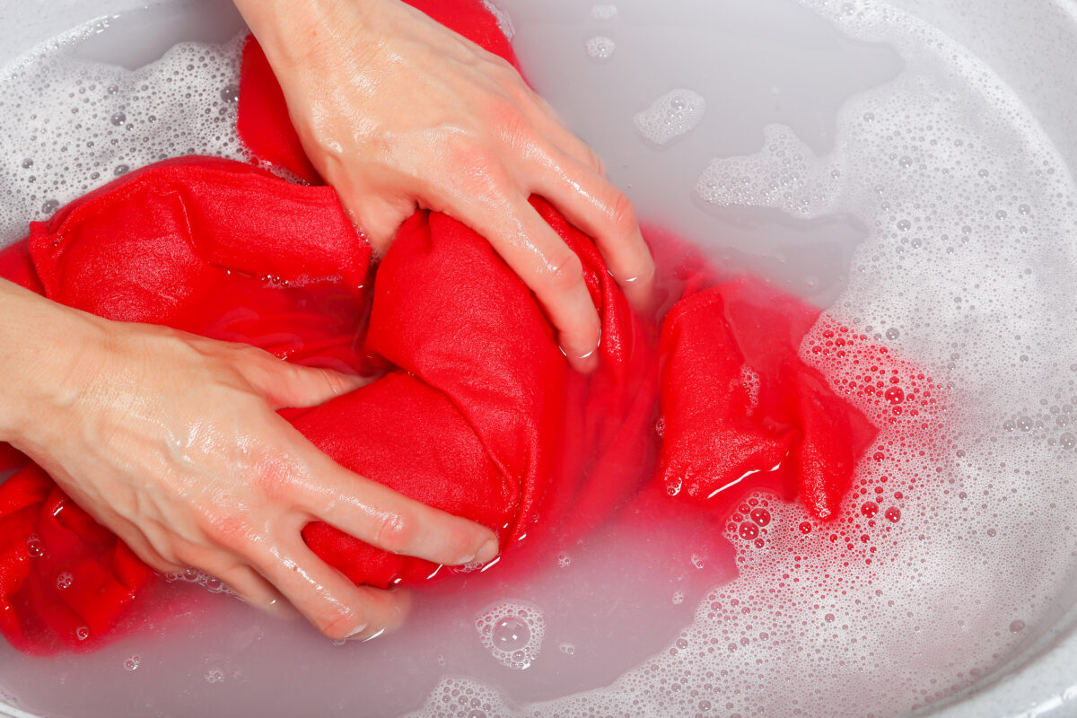 hands washing a red garment in a sink