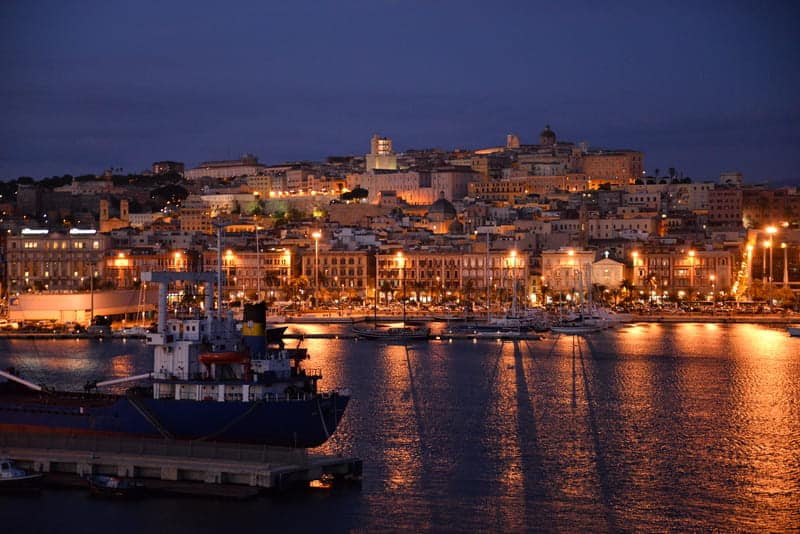 City of Cagliari at night. 3-day itinerary for Sardinia. City lights and boats in the water in the evening.