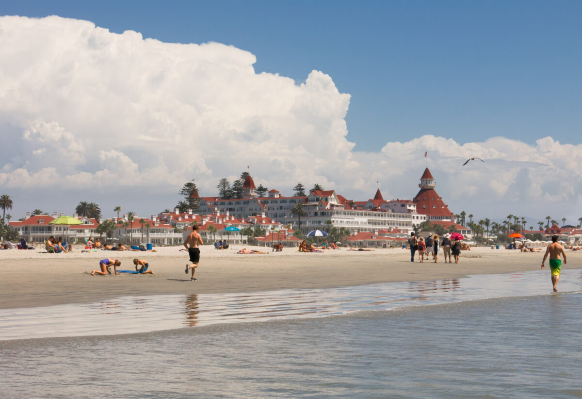 Coronado Beach in San Diego. People at the beach walking and running along the coast with sunbathers on the sand