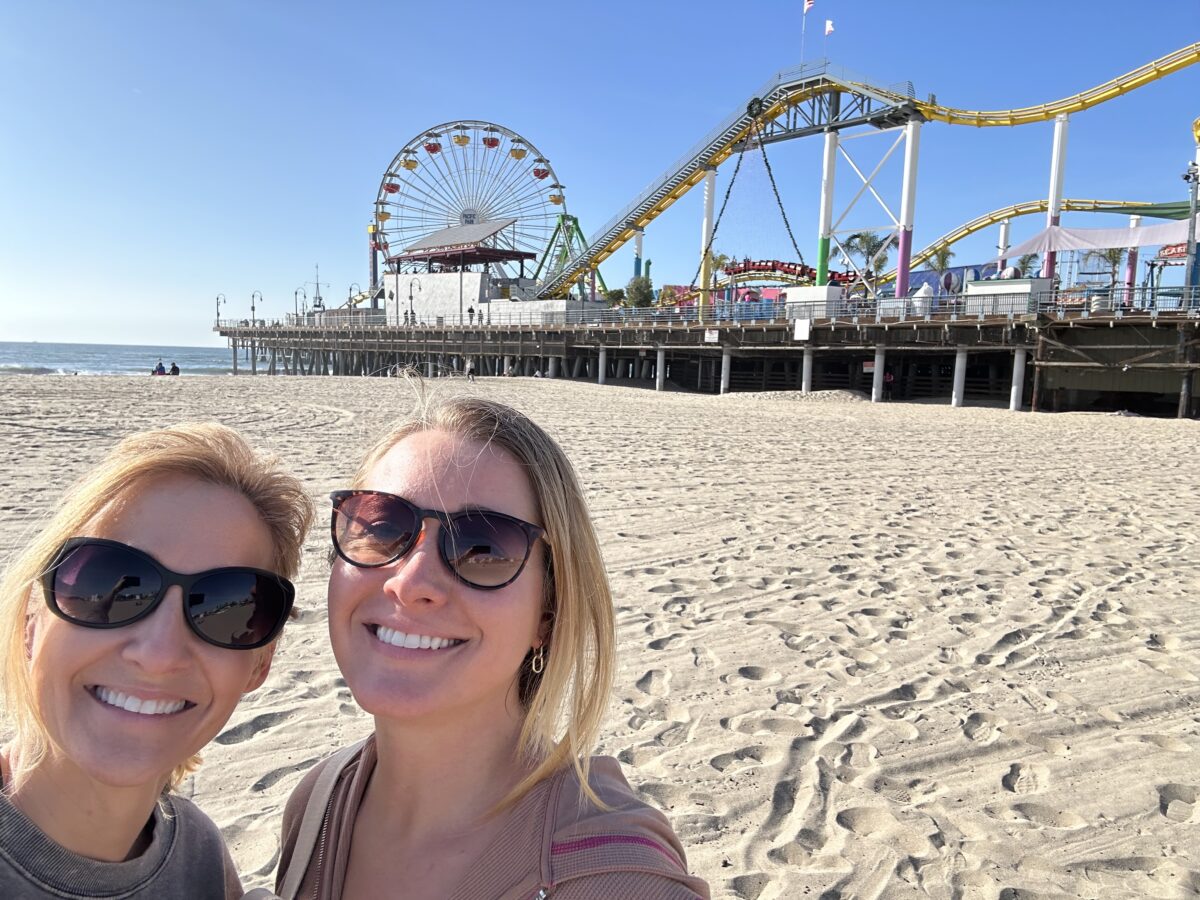 Two women at Santa Monica Beach with a view of the Santa Monica roller coaster and pier in the background