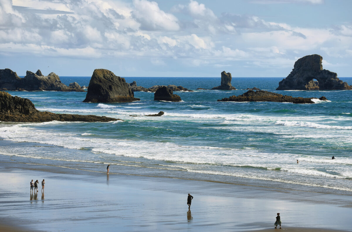 people standing on the sand with waves crashing on Indian beach in Ecola State Park