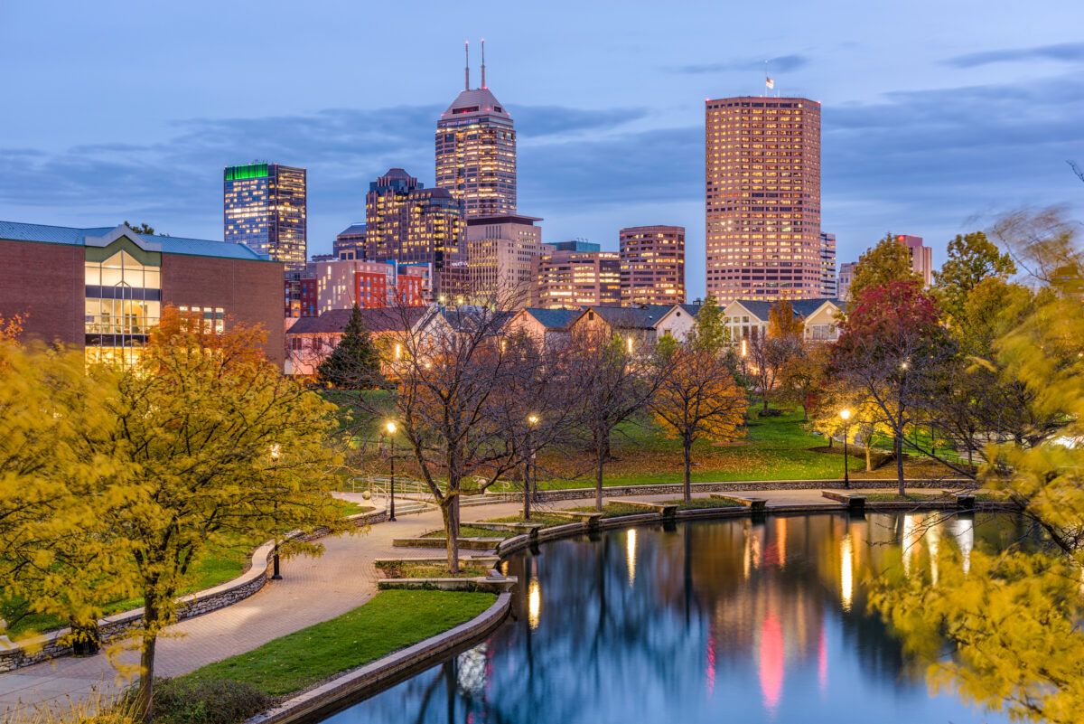 Picture of Indianapolis, Indiana in the fall at evening. City skyline in the distance. Showing a walking path and lights reflecting off the canal.