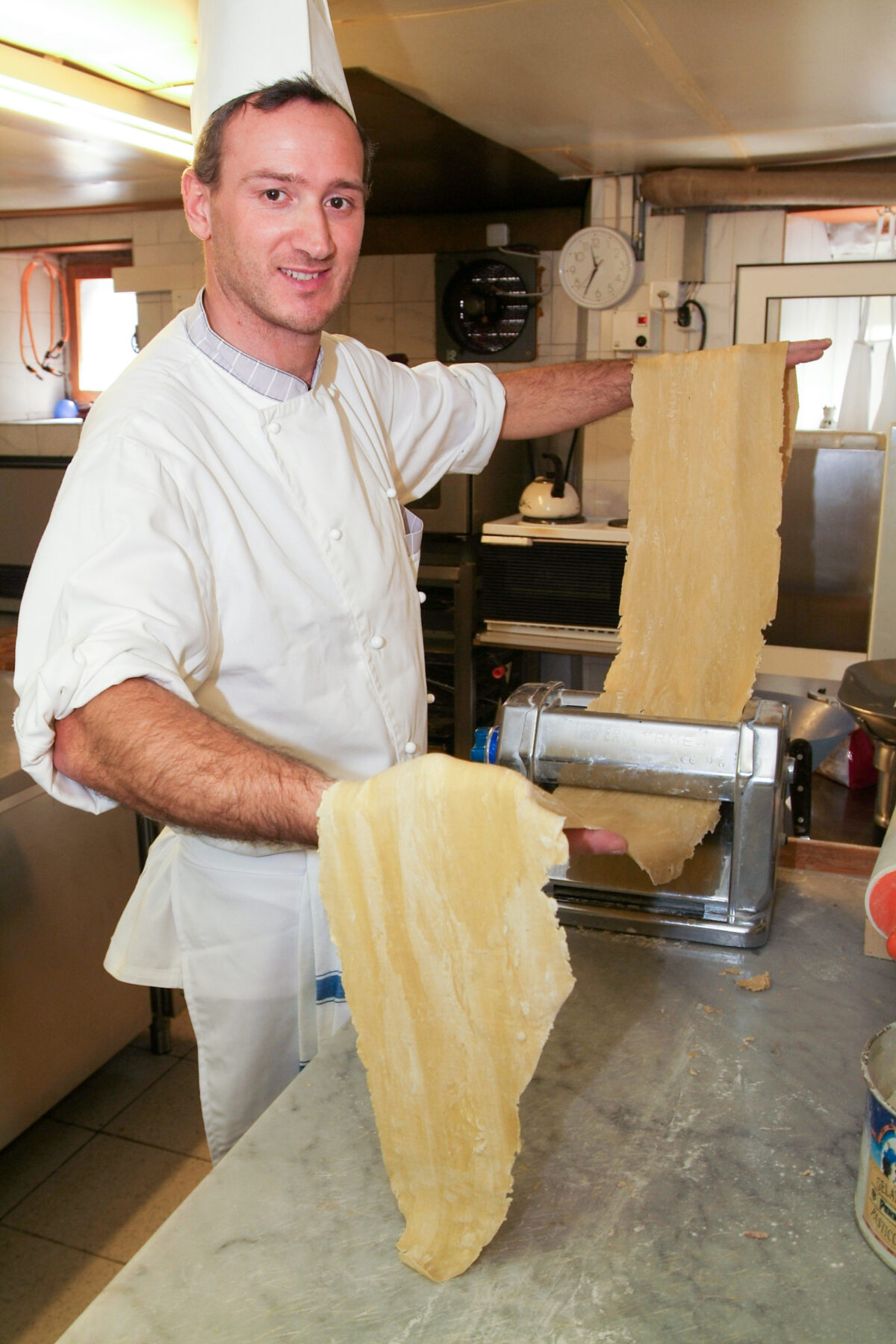 Chef running dough through a pasta machine making fresh pasta