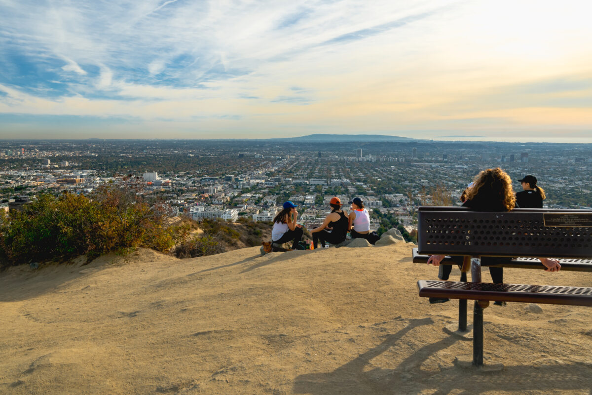 Hikers at the top of a mountain peak in California. three hikers sitting overlooking Sanat Monica. One woman sitting on a metal bench.