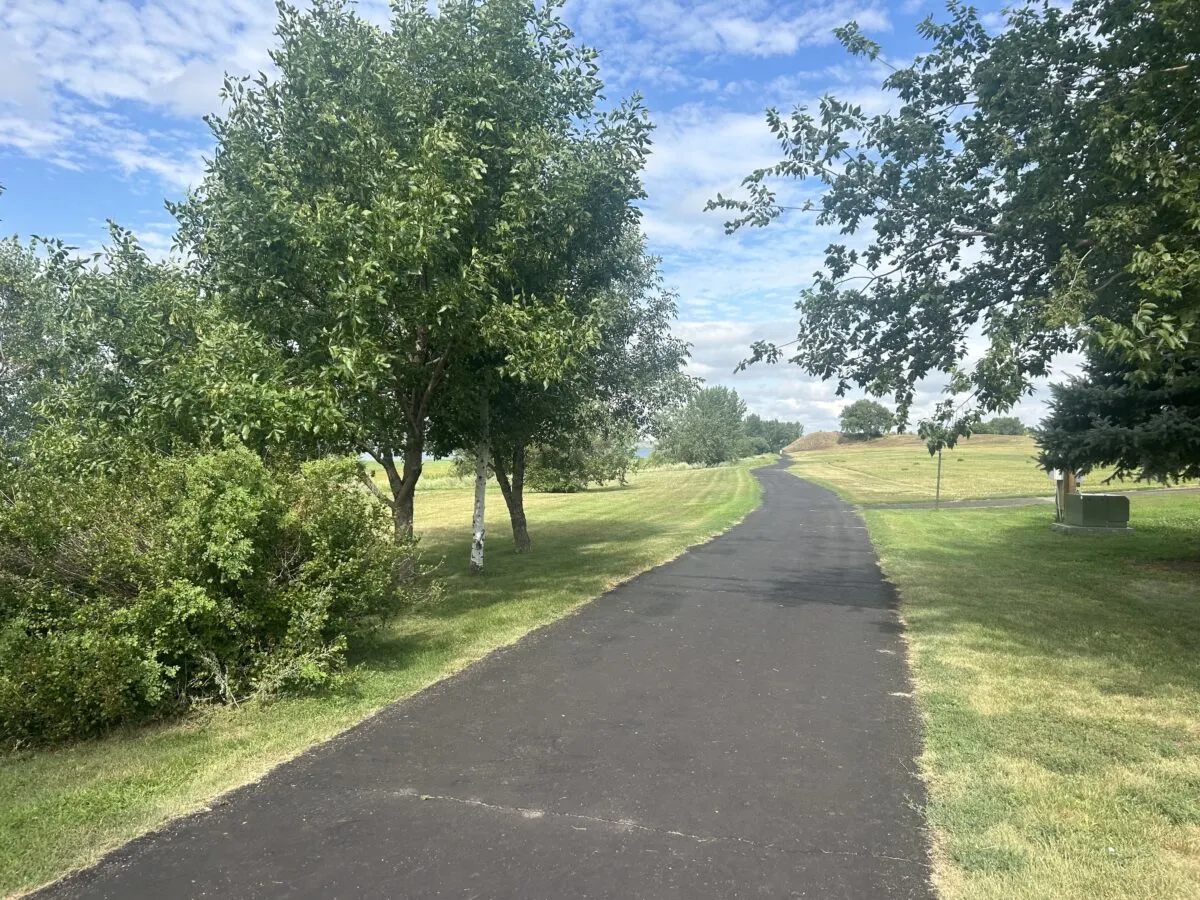 A paved trail in Mobridge. Part of the Lewsi and Clark Trail. A sunny day with trees along the path.