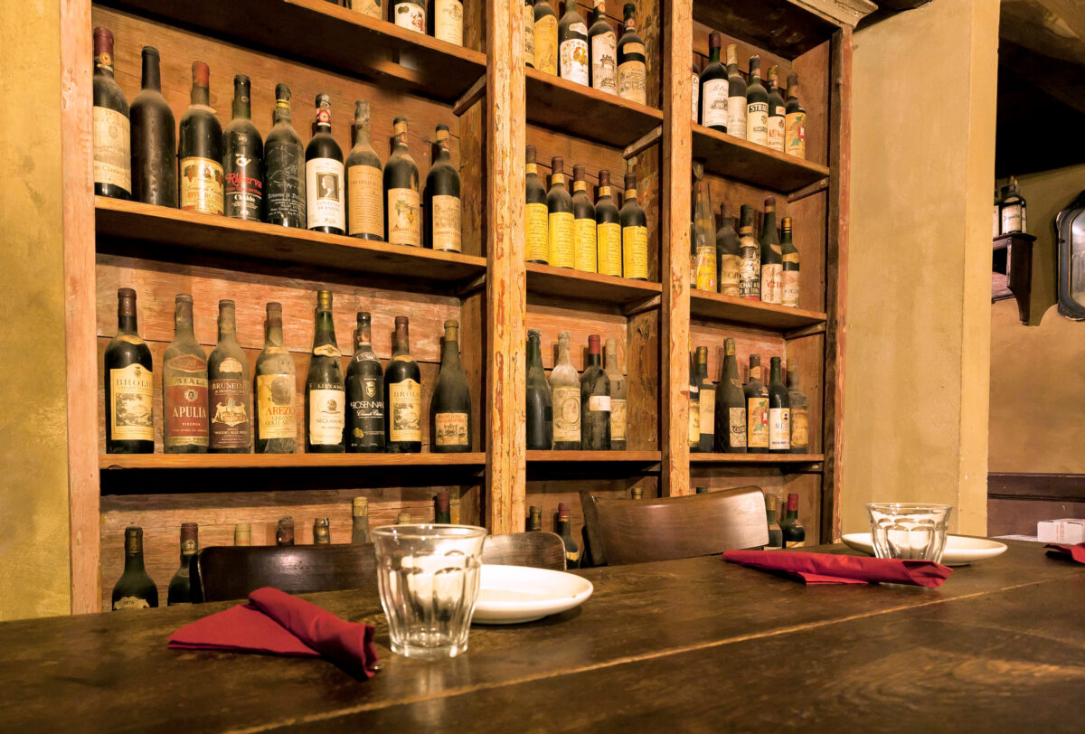 Italian restaurant bar with plates and glasses set out awaiting guests. Bottles of wine lining the back wall behind the bar