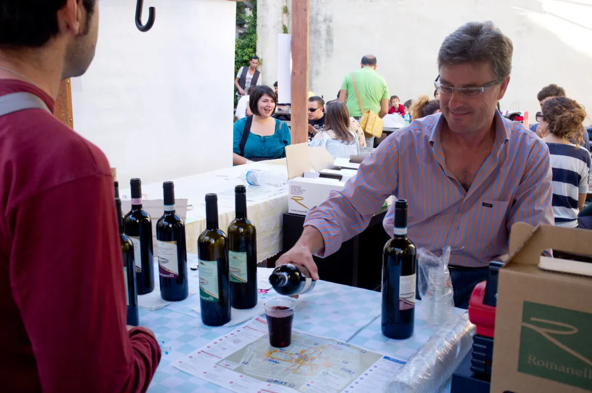 Man pouring a wine sample into a cup for another man.