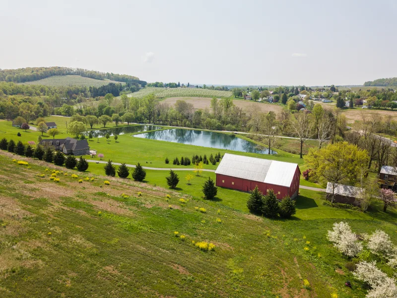 aerial shot of farm with red barn and lake