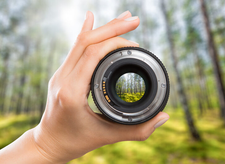 woman's hand holding camera lens with trees