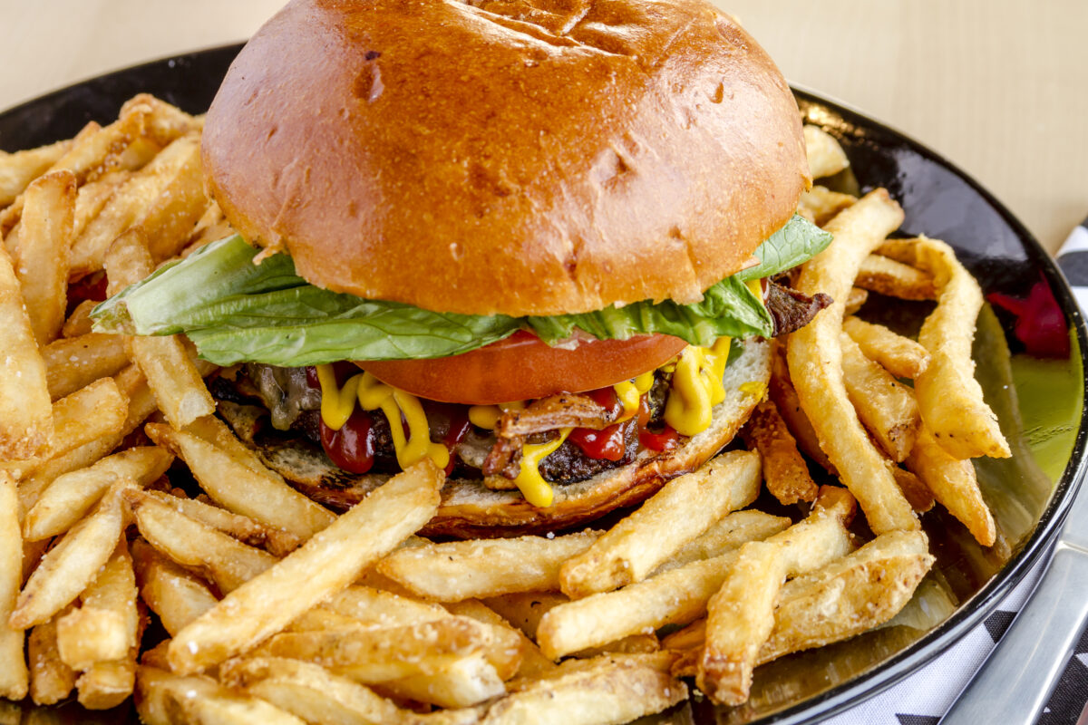 Gourmet hamburger setting on a plate with a bun with lettuce, tomato, mustard and catsup surrounded by a sea of fresh fries