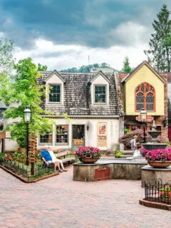 a town square with a yellow and gray house surrounded blow flowers