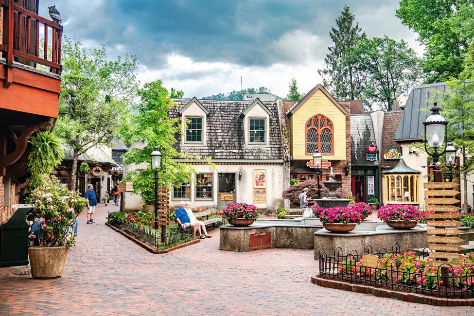 a town square with a yellow and gray house surrounded blow flowers