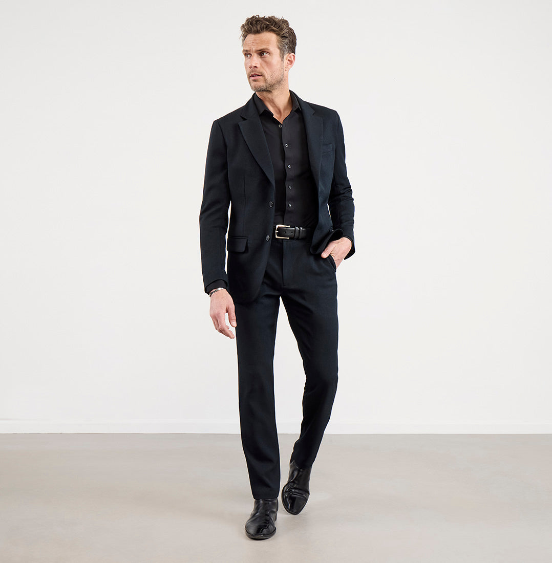 A man wearing the Bluffworks Gramercy 2.0 travel blazer in asphalt black with matching trousers
