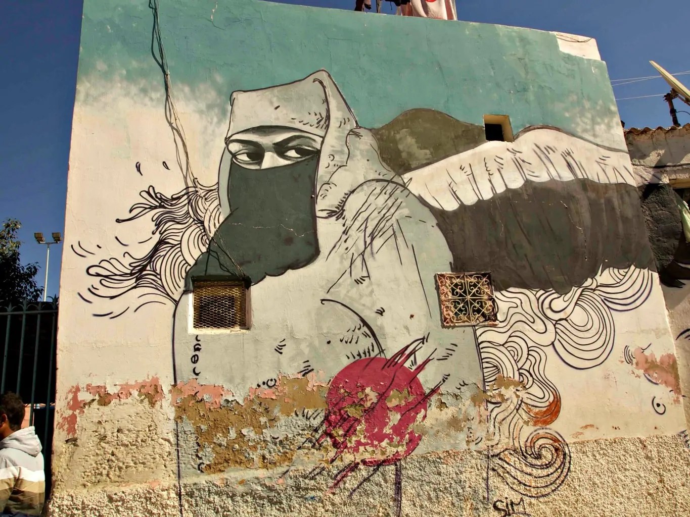 Street art of a woman in a burqa with wings behind her. She is staring out the side of her eyes. 
