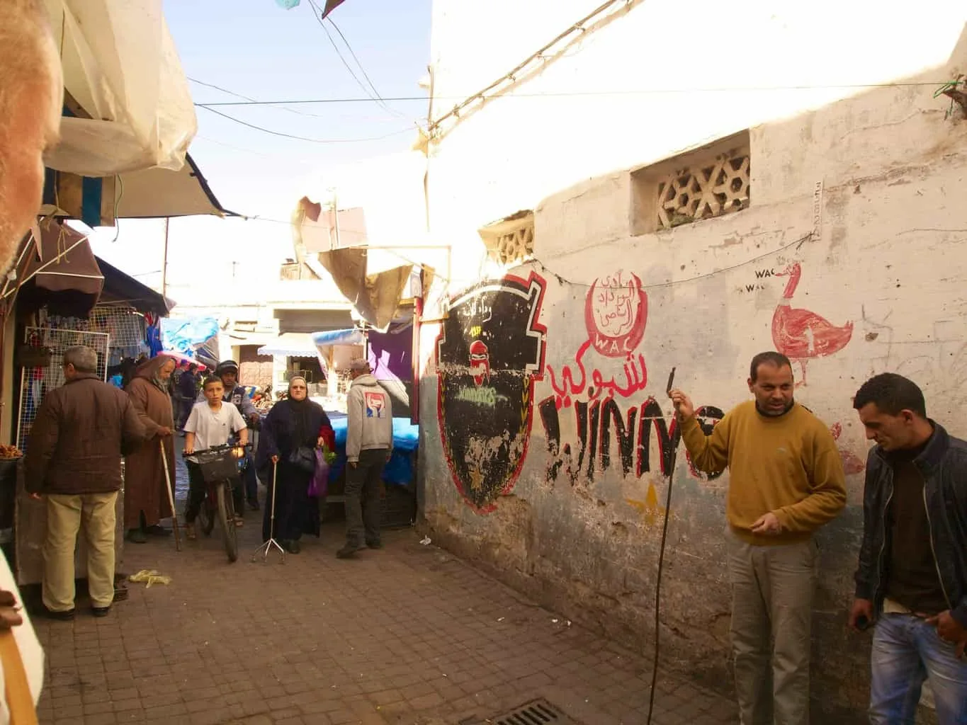 People standing in the alleyway of a market in Casablanca, with street art on a wall behind them. 

